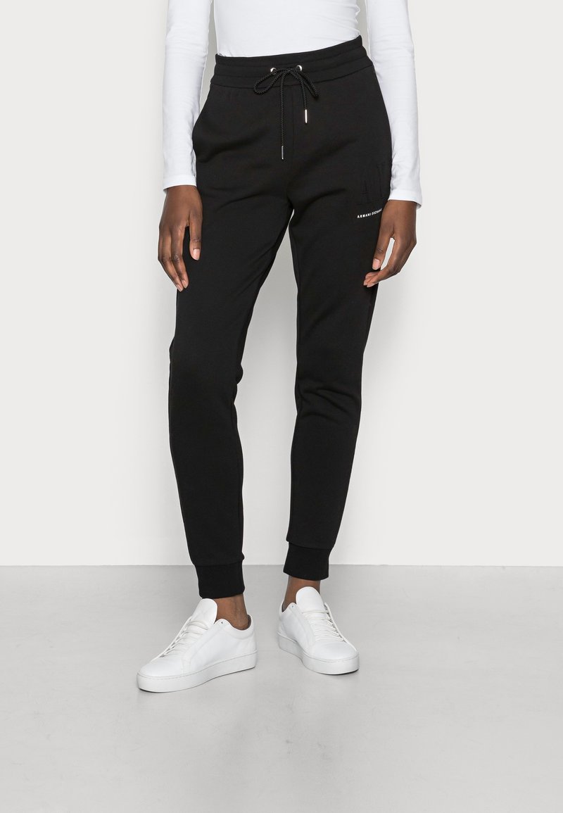 Svarta träningsoverallsbyxor i mjukt tyg, med dragsko i midjan, avsmalnande ben, ribbade mudd och sidofickor. Tillsammans med vita sneakers.