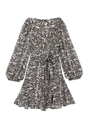 Kobieta ubrana w sukienkę w paski zebry, z czarną teksturowaną kurtką zarzuconą na ramiona oraz czarne botki do połowy łydki z metalowymi detalami.