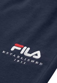Navy blue polar materiał z haftowanym białym i czerwonym logo "FILA" oraz białym napisem "ESTABLISHED 1911" poniżej logo. Miękka tekstura.