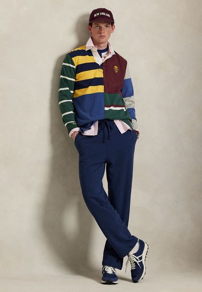 Daugiakoloris regbio marškinėlis su žaliais, mėlynais, geltonais ir tamsiai raudonais dryžiais; derinamas su tamsiai mėlynomis sportinėmis kelnėmis ir pilkais sportbačiais. Burgundinės spalvos kepuraitė su užrašu „NEW ENGLAND“.