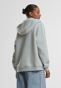 Lys grå hettegenser med avslappet passform, snor i hetten og ribbede ermer. Myk tekstur, ingen synlige mønstre, parret med løse denimjeans.