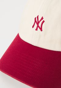 Cappellino regolabile con una parte frontale in tessuto crema e visiera rossa. Presenta un logo ricamato rosso sul davanti e la parte inferiore della visiera texturizzata in rosso.