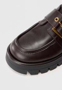 Pruun nahkne king, millel on paks must tald, ümar varvas, dekoratiivne rihm ja kuldse sära aktsendid. Sile tekstuur.