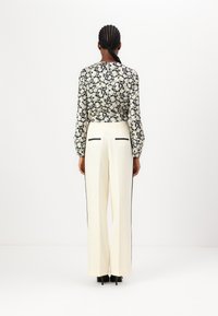 Blusa a maniche lunghe con motivo floreale in nero e crema, abbinata a pantaloni larghi crema con strisce laterali nere e tasche posteriori.
