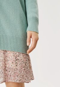 Světlemodrý pletený svetr s žebrovanými manžetami a lemem, spárovaný s růžovou sukní s květinovým vzorem a rozšířeným střihem.