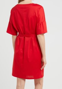 Vestido de algodón rojo con mangas cortas con volantes, un escote redondo y un cinturón de tela. La vista trasera muestra un diseño simple y ajustado con pliegues.