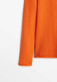 Manche et ourlet d'un pull en tricot orange à manches longues sur fond blanc, montrant une texture douce et des détails de couture simples.