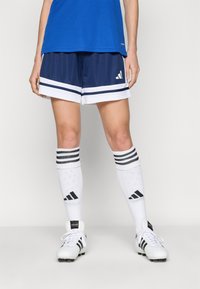 Adidas blå skjorta med marinblå shorts som har vita ränder, i kombination med vita strumpor med svarta ränder och skor med svarta accenter.