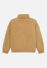 Beige letvægtsjakke med elastiske manchetter og talje, stående krave og lille logo-detalje på bagsiden af halsen.