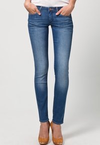 Smal blå denimjeans med medelton, fem fickor och knappstängning. Bärs med tanfärgade vävda högklackade skor, slät textur.