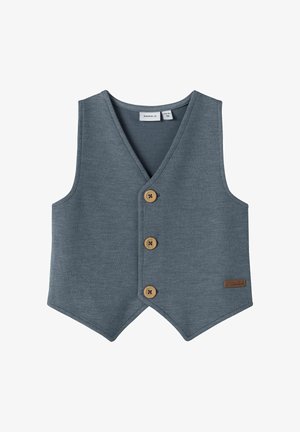 Gilet gris texturé avec un col en V, comportant trois boutons en bois et une petite étiquette en cuir sur le côté. Conception sans manches, ajustée.