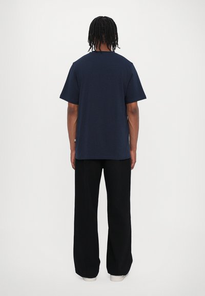 Camiseta de algodón azul marino con mangas cortas, cuello redondo clásico y corte relajado, combinada con pantalones de pierna ancha negros y zapatos blancos.