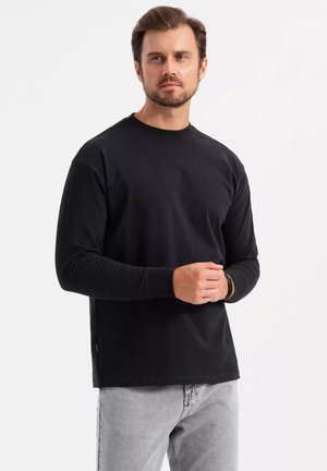Zwarte lange mouw shirt met een ronde hals, gemaakt van zachte stof. Beschikt over een comfortabele pasvorm en subtiele stikdetails aan de zijkanten.