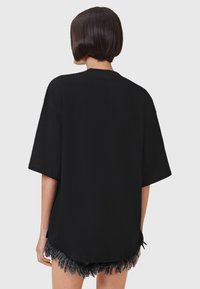 Camiseta negra de gran tamaño con mangas cortas, hecha de una tela suave. Presenta un escote redondeado y un dobladillo recto, mostrando pantalones cortos con flecos por debajo.
