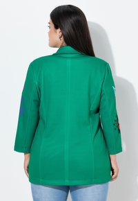 Groene blazer met driekwartmouwen. Heeft kleurrijke borduursels op de mouwen, een gladde textuur en een getailleerde pasvorm. Achteraanzicht getoond.