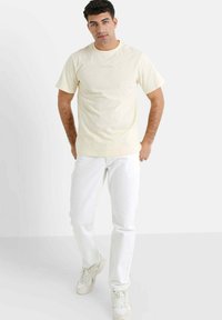Creme farvet bomulds T-shirt med korte ærmer og rund halsudskæring. Sammen med hvide denim jeans og lyse sneakers.