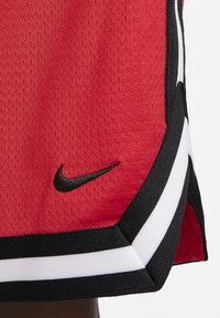 Punane spordisärk tekstuurse kangaga, mustade ja valgete aktsentidega ning must Nike'i logo allääres.