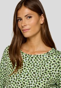 Grünes und weißes Langarmoberteil mit einem Leopardenmuster in Schwarz und Dunkelgrün, glatte Textur und runder Ausschnitt.