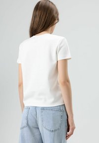 Witte top met korte mouwen en een ronde hals, gecombineerd met lichtblauwe, loszittende denim shorts met achterzakken en zichtbare naden.