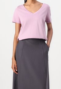 Ljusrosa t-shirt med V-ringning i mjukt bomull, tillsammans med en mörkgrå högmidjad kjol. Kjolen har fickor och en slät yta.