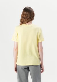 T-shirt en coton jaune à manches courtes et col rond. Présente des fentes latérales à l'ourlet, vue de l'arrière.