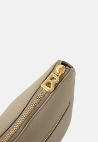 Borsa a tracolla in pelle beige con finitura testurizzata, presenta una zip e dettagli in oro, e una tasca laterale con una simile finitura della zip.