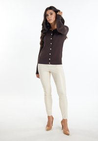 Bruine lange mouwen cardigan met een slim fit, voorzien van parelachtige knopen aan de voorkant. Gecombineerd met crèmekleurige, aansluitende broeken.