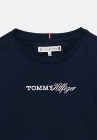 Μπλε ναυτικό βαμβακερό μπλουζάκι με στρογγυλή λαιμόκοψη, με λευκό κεντημένο λογότυπο "TOMMY HILFIGER". Ορατή ετικέτα με πληροφορίες για το εμπορικό σήμα.