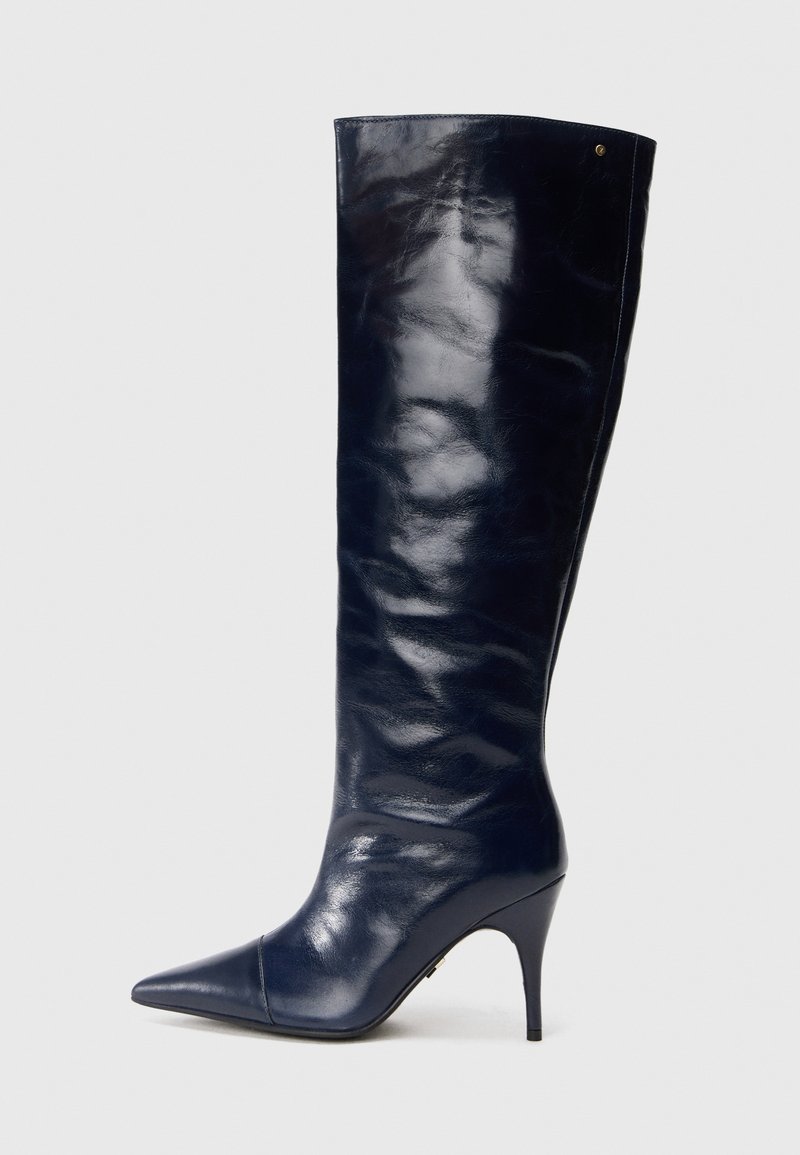 Navy leather knee-high boot, glossy finish, pointed toe, slim stiletto heel, seamless design, features a subtle gold accent.