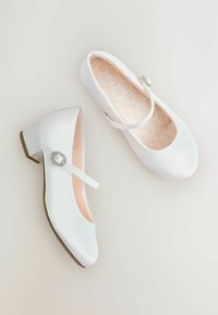 Białe baletki z błyszczącym wykończeniem, zaokrąglonym noskiem i niskim szerokim obcasem. Posiadają pasek z ozdobną owalną klamrą.