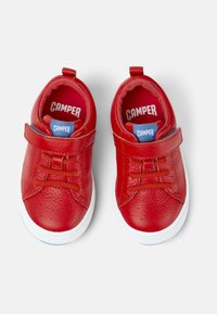 Chaussures en cuir rouge avec une finition texturée, dotées d'une sangle Velcro, de lacets et d'une semelle en caoutchouc blanc. Marquage "CAMPER" bleu et blanc à l'intérieur.