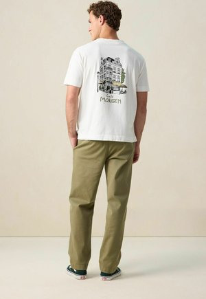 Witte katoenen t-shirt met een afbeelding van een gebouw en de tekst "Café Morgen", gecombineerd met olijfgroene broek en donkere sneakers.