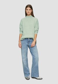 Mintgroene ribgebreide trui met hoge hals, gecombineerd met lichtblauwe flared jeans en metallic zilveren enkellaarsjes. Simpel ontwerp, comfortabele pasvorm.