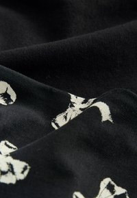Svart tyg med en mjuk textur, med ett vitt abstrakt mönster. Materialet ser något skrynkligt ut, vilket framhäver dess drapering och rörelse.