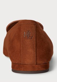 Hnedé semišové slip-on topánky s okrúhlou špičkou; majú zvýšený šev na päte a malé vyrazené logo na zadnej strane. Hladká podošva.