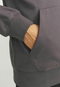Donkergrijze sweatshirt met een kangoeroezak, ribbelmanchetten en een gladde textuur. De stof lijkt zacht en iets rekbaar.