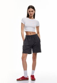 Camiseta blanca ajustada, pantalones cortos gris carbón con cintura elástica y bolsillos, combinados con zapatillas rojas y calcetines blancos.