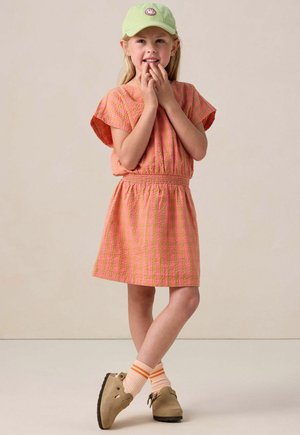 Robe rayée rose et orange avec des manches courtes et une ceinture élastique, accompagnée d'une casquette verte et de chaussures marron, avec des chaussettes rayées.