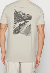 Krémové tričko s krátkým rukávem, na zadní straně s potiskem černobílé horské krajiny a logem "Columbia Sportswear Company".