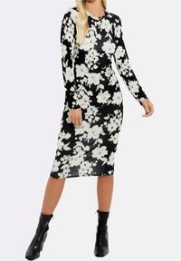 Svart långärmad klänning med ett vitt blommönster, figurnära design, knälång, mjuk textur, tillsammans med svarta ankelboots.