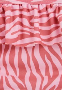 Tissu à motif de zèbre rose et rouge avec une section froncée et volée le long du bord supérieur.