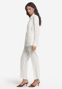 Vit linnekavaj med slag och skört, matchad med löst sittande byxor i samma färg. Bruna öppna klackskor fulländar looken. Mjuk textur, enkel design.