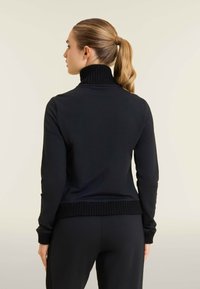 Jersey negro de cuello alto, fabricado en un tejido suave con puños y dobladillo acanalados, que presenta una silueta ajustada, visto desde la parte trasera.