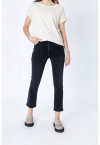 Camiseta de algodón beige con mangas enrolladas, combinada con jeans cortos negros y mocasines beige con un diseño texturizado.