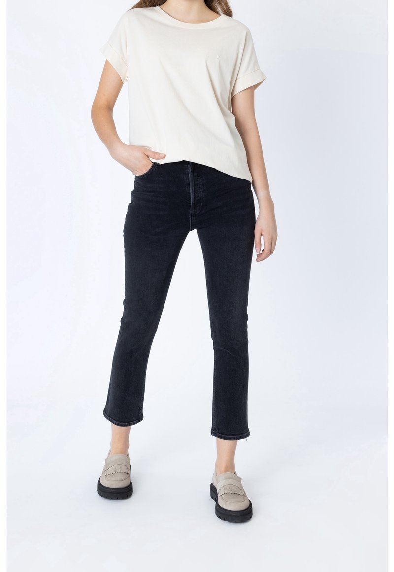 Camiseta de algodón beige con mangas enrolladas, combinada con jeans cortos negros y mocasines beige con un diseño texturizado.