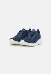 Scarpe da ginnastica blu navy con una tomaia in maglia testurizzata, suola bianca, design con lacci e linguette sul tallone per indossarle facilmente.