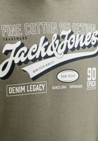 Logo et texte Jack & Jones sur tissu mentionnant coton fin, héritage denim, indigo brut, Barcelone, Copenhague et époque des années 90.