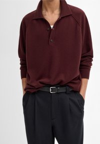 Bordeaux lange mouwen polo shirt met een puntkraag, twee knopen en ribgebreide manchetten, gecombineerd met op maat gemaakte zwarte broeken en een zwarte riem.