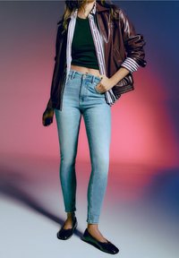 Smala jeans i ljusblå denim, kombinerade med en mörk croptop, lager på lager med en brun läderjacka och randig skjorta. Svarta ballerinaskor.