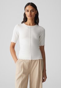 Witte, ribbelige top met korte mouwen, afgeronde halslijn en gegolfde randen, met een centrale naad en een getailleerde pasvorm.